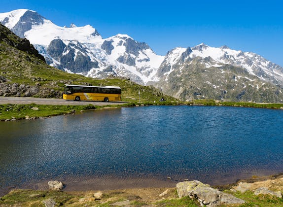 Sustenpass: Perjalanan Postauto di sepanjang tasik dengan gunung berpasir di latar belakang, Switzerland.