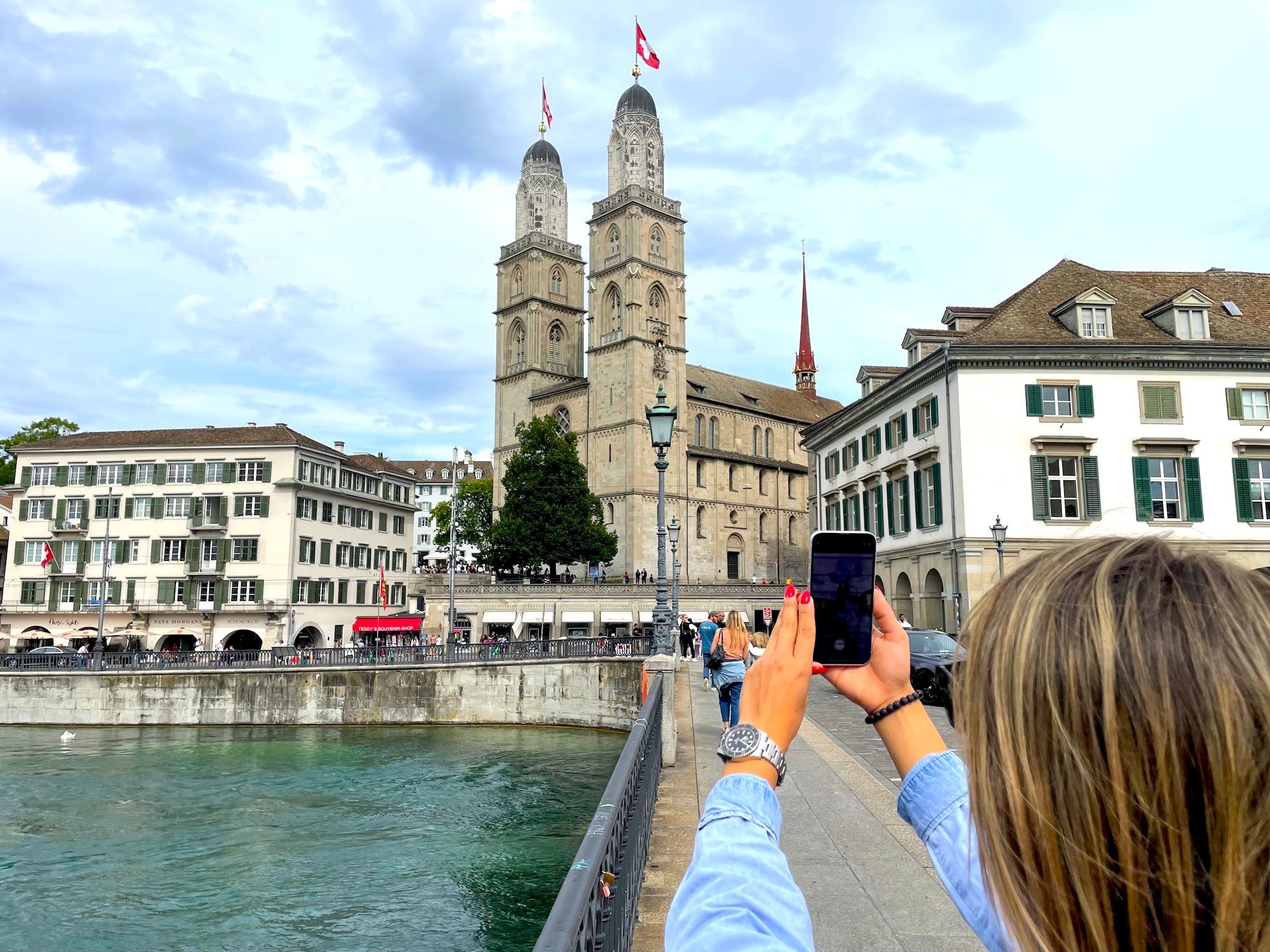 Zúrich: Mujer fotografiando el Grossmünster a orillas del lago de Zúrich en un día soleado.