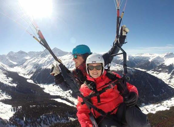 Gleitschirmfliegen in Klosters mit Blick auf die schneebedeckten Berge im Winter. Erlebe den Nervenkitzel.
