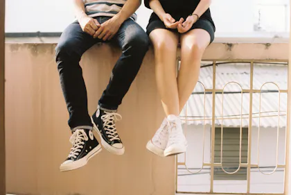 Zwei Personen sitzen an einem Fenster und tragen Sneakers.