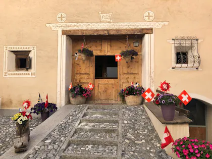 Haus Eingang in Engadin mit Blumen und Schweizer Flaggen, idyllische Umgebung, Natur genießen.
