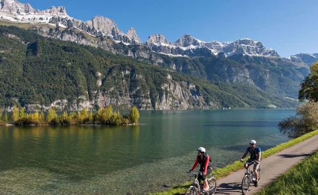 Walenseeufer con ciclistas, montañas al fondo y agua clara.
