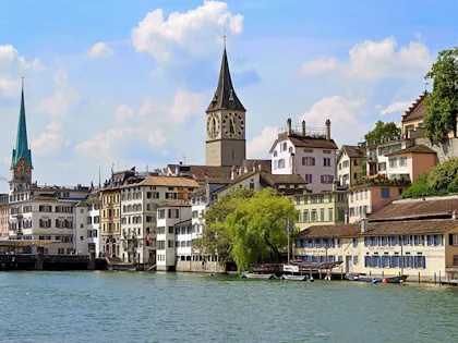 Zürich: malerische Altstadt am Wasser mit historischen Gebäuden und üppigem Grün im Sommer.