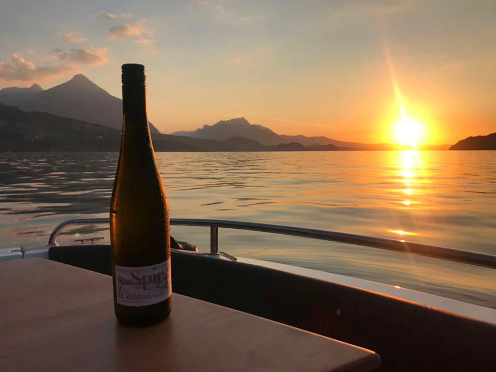 Flasche Wein auf Boot, Sonnenuntergang über See, Berge im Hintergrund