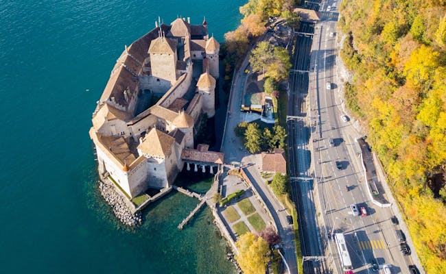 Schloss Chillon mit Blick auf den Genfersee und herbstliche Bäume.