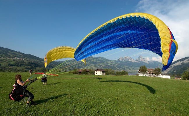 Parapendio a Horgen, i piloti decollano con colorate vele, verde intenso e montagne sullo sfondo.