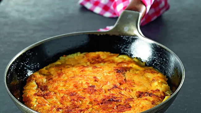 Rösti na pánvi, zlatavá a křupavá, na tmavém stole