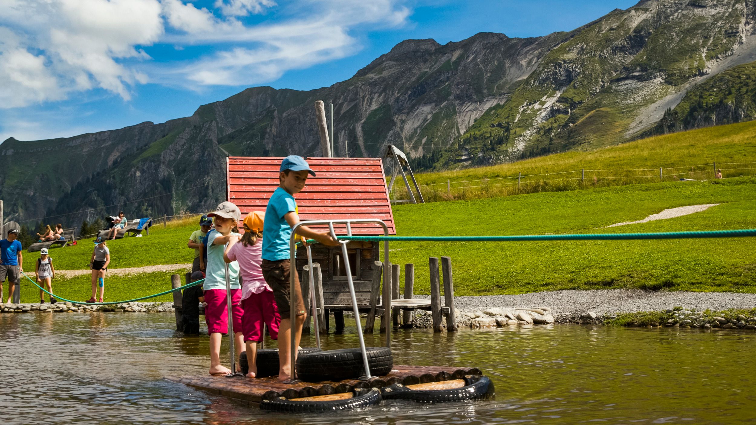 Mooraculum: Barn leker på en flotte vid Rossweid Sörenberg under sommaren, omgiven av natur.