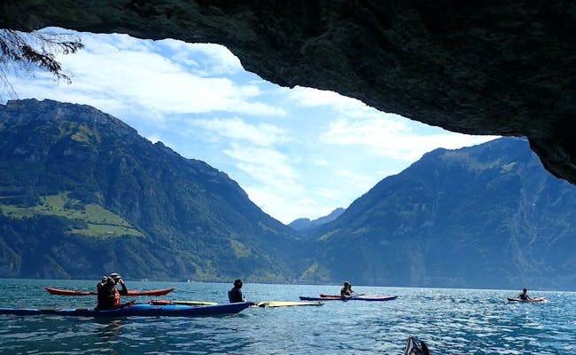 Vierwaldstättersee-hulen med kajaksejler, omkringliggende bjerge og blå himmel.