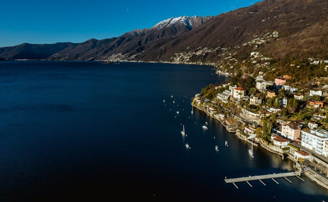 Lago Maggiore: pemandangan romantis dengan gunung, kapal layar, dan air jernih di musim panas.