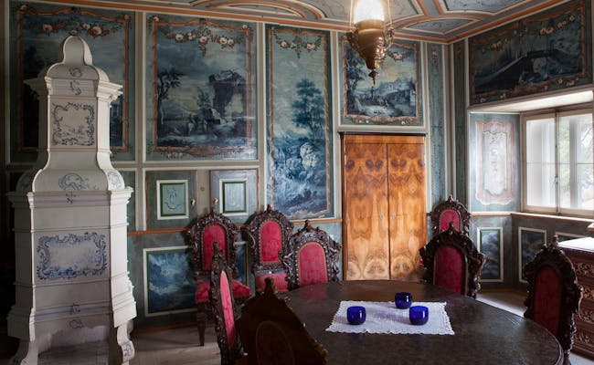 Chesa Planta-museet med blå väggar, antika möbler, röda stolar och ett runt bord.
