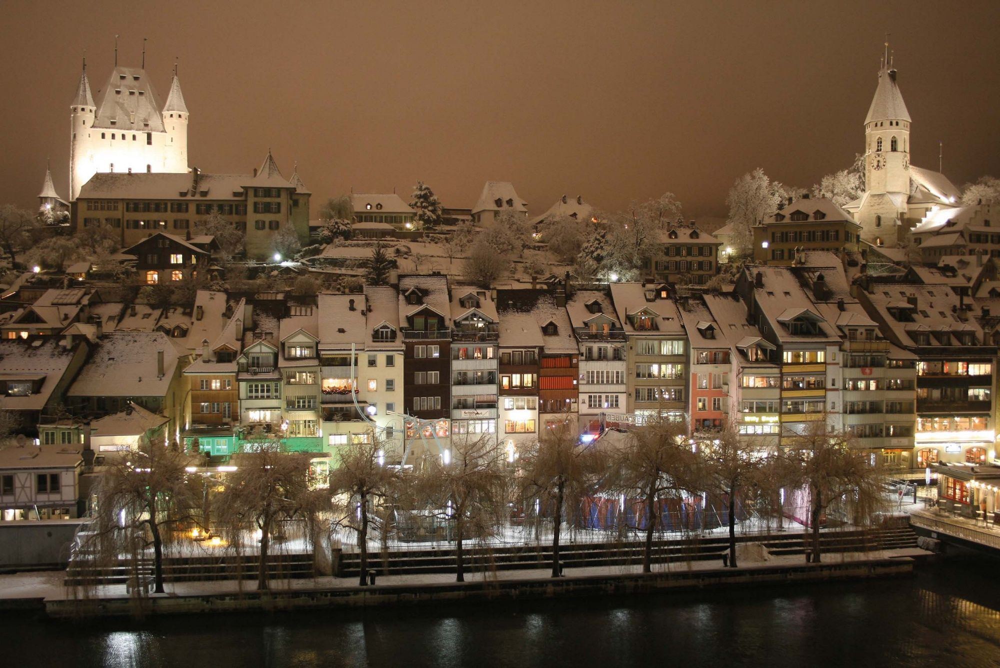 Thun : Vue hivernale de la ville avec des maisons enneigées et un paysage fluvial romantique.