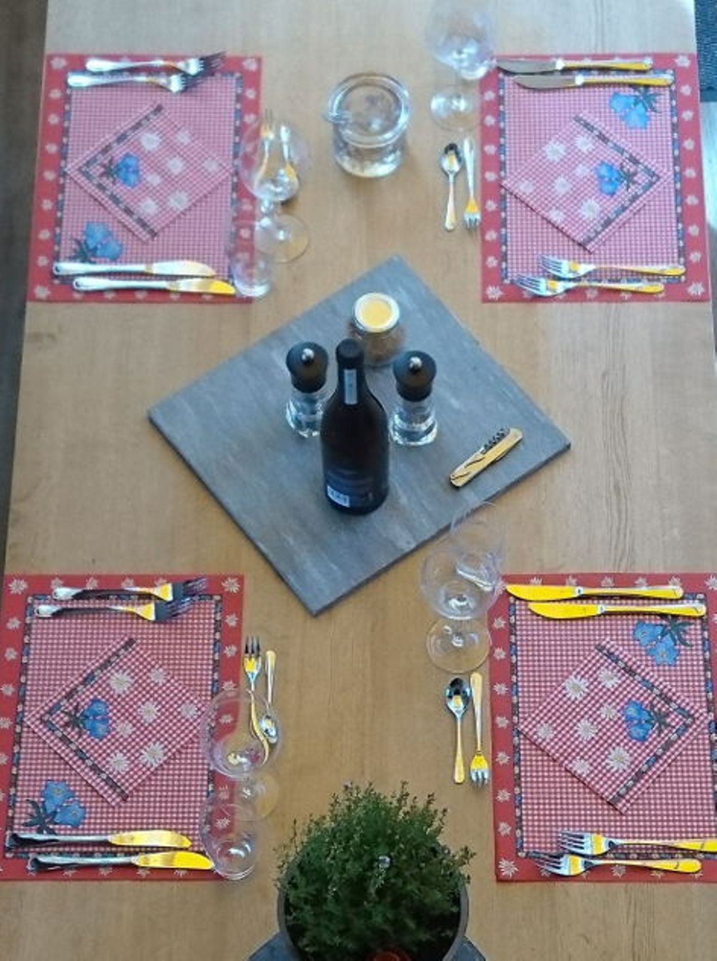 Decoração de mesa aconchegante com toalhas de mesa xadrez vermelhas e talheres. Elementos sazonais e plantas ao fundo.