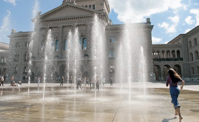 Bundesplatz Berna con fontana e persone che giocano in una giornata di sole