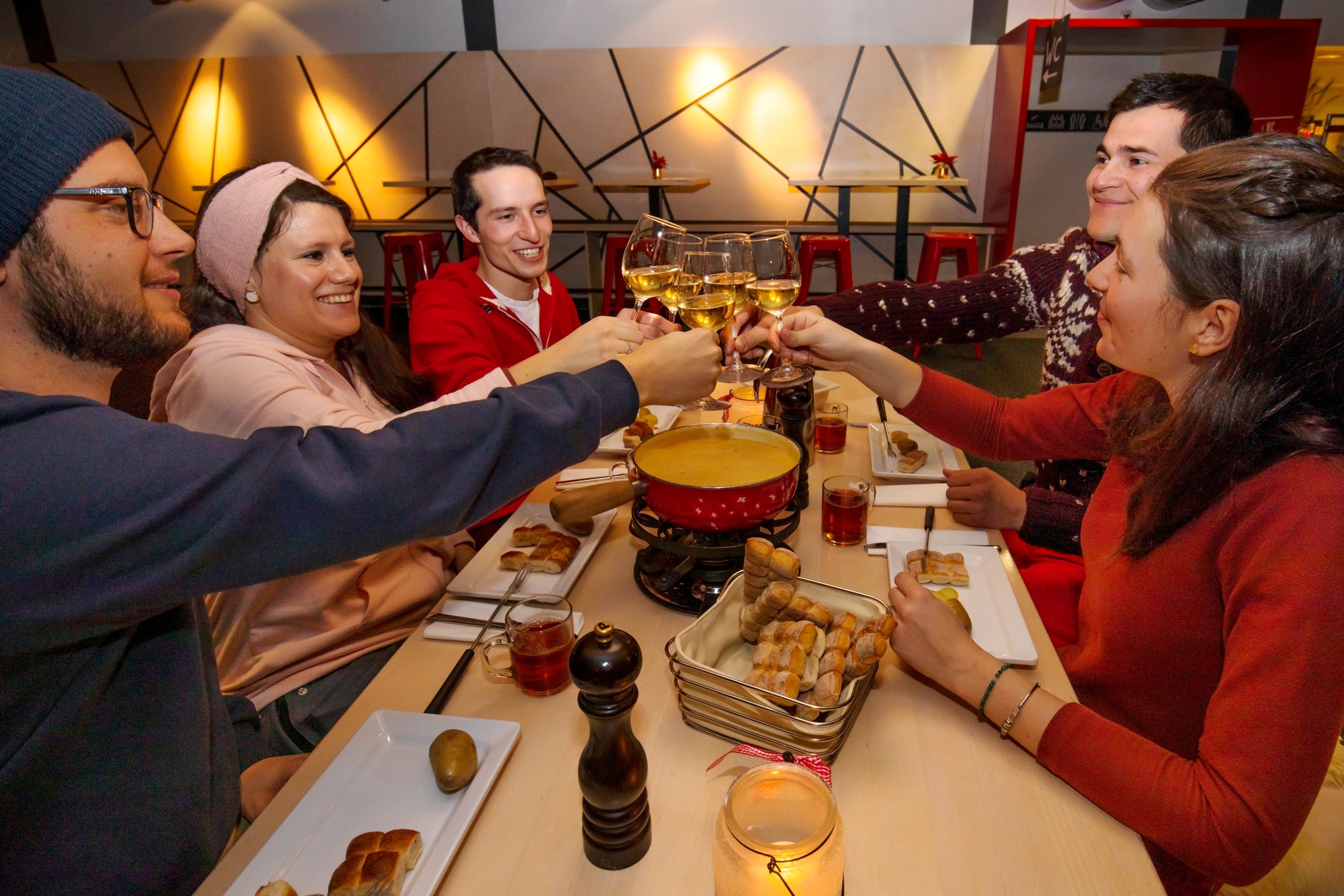Весёлая компания на вечеринке с фондю на Нижерхорне, поднимающая бокалы. Уютная атмосфера с фондю и вкусной едой.
