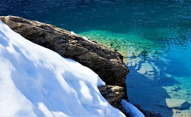 冬季的卡乌马湖:覆盖着雪的岩石和清澈的蓝色湖水。