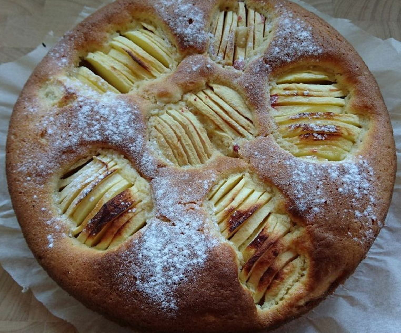 Bolo de maçã com maçãs fatiadas e açúcar em pó.