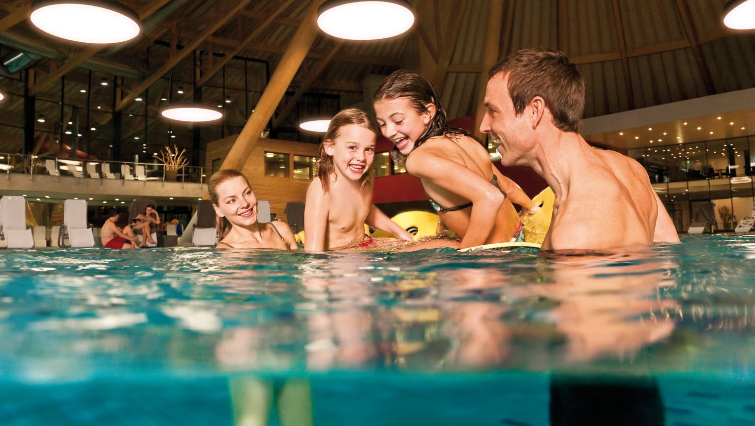 Family members are playing in the Aquabasilea water park, swimming and laughing.