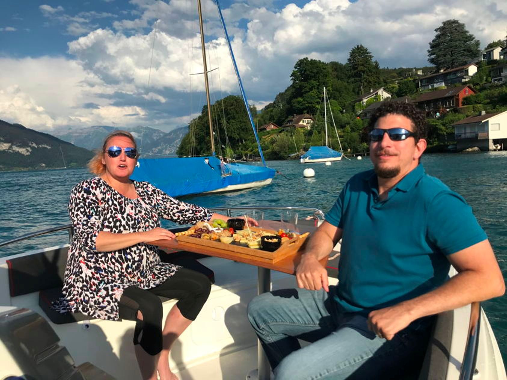 호수 한가운데 보트 위에서 두 사람이 치즈와 와인을 즐기고 있어요.