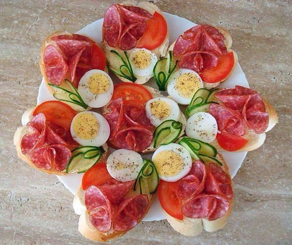 Sicilian food with open sandwiches, salami, eggs, and vegetables on a plate.