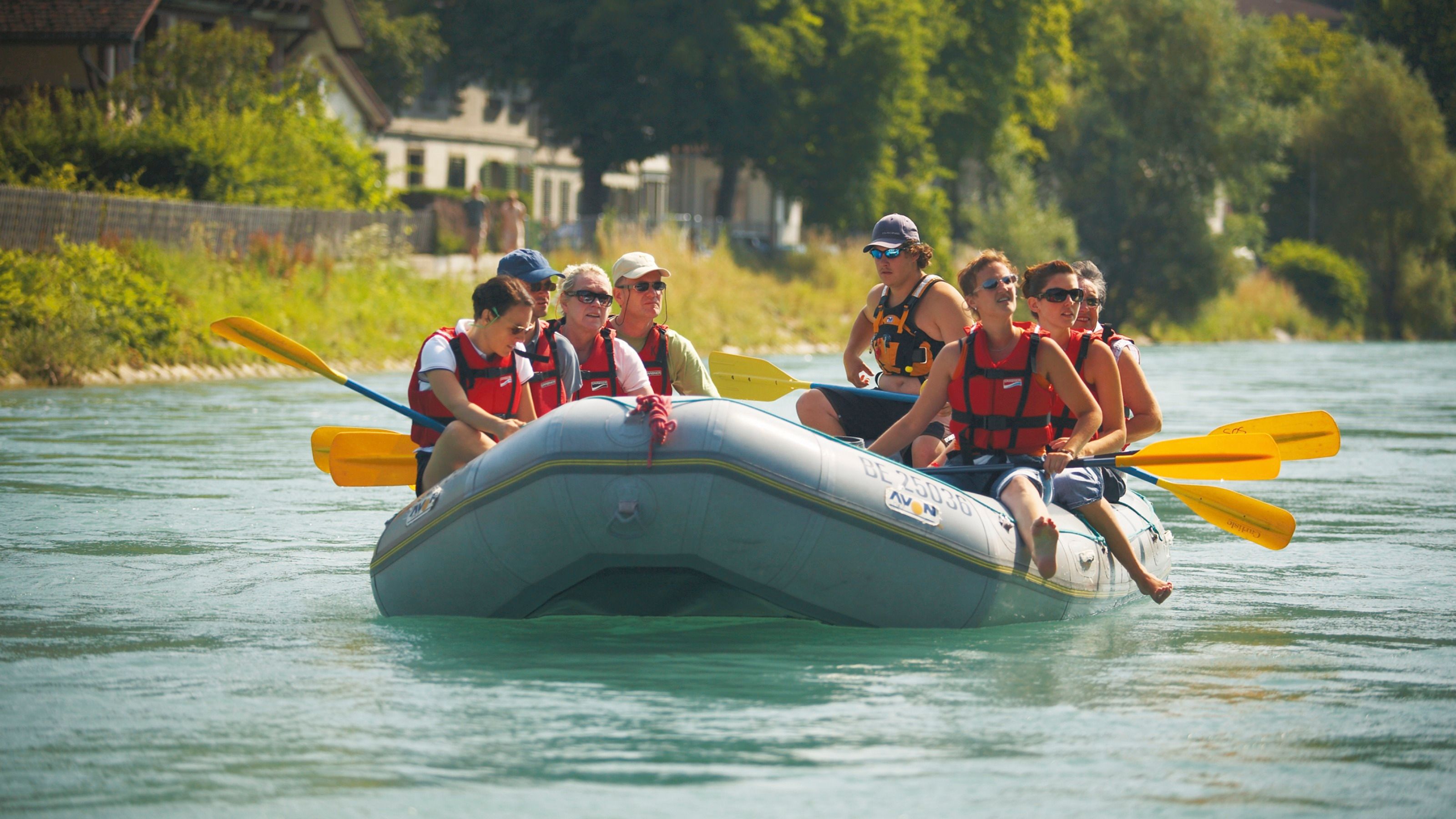 रेड वेस्ट पहने कई व्यक्तियों के साथ बर्न में पानी पर नाव की यात्रा।