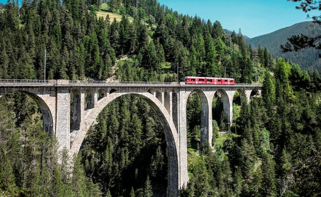 Wiesenviadukt der Rhätischen Bahn in Davos mit rot-gelbem Zug in der Zügenschlucht.