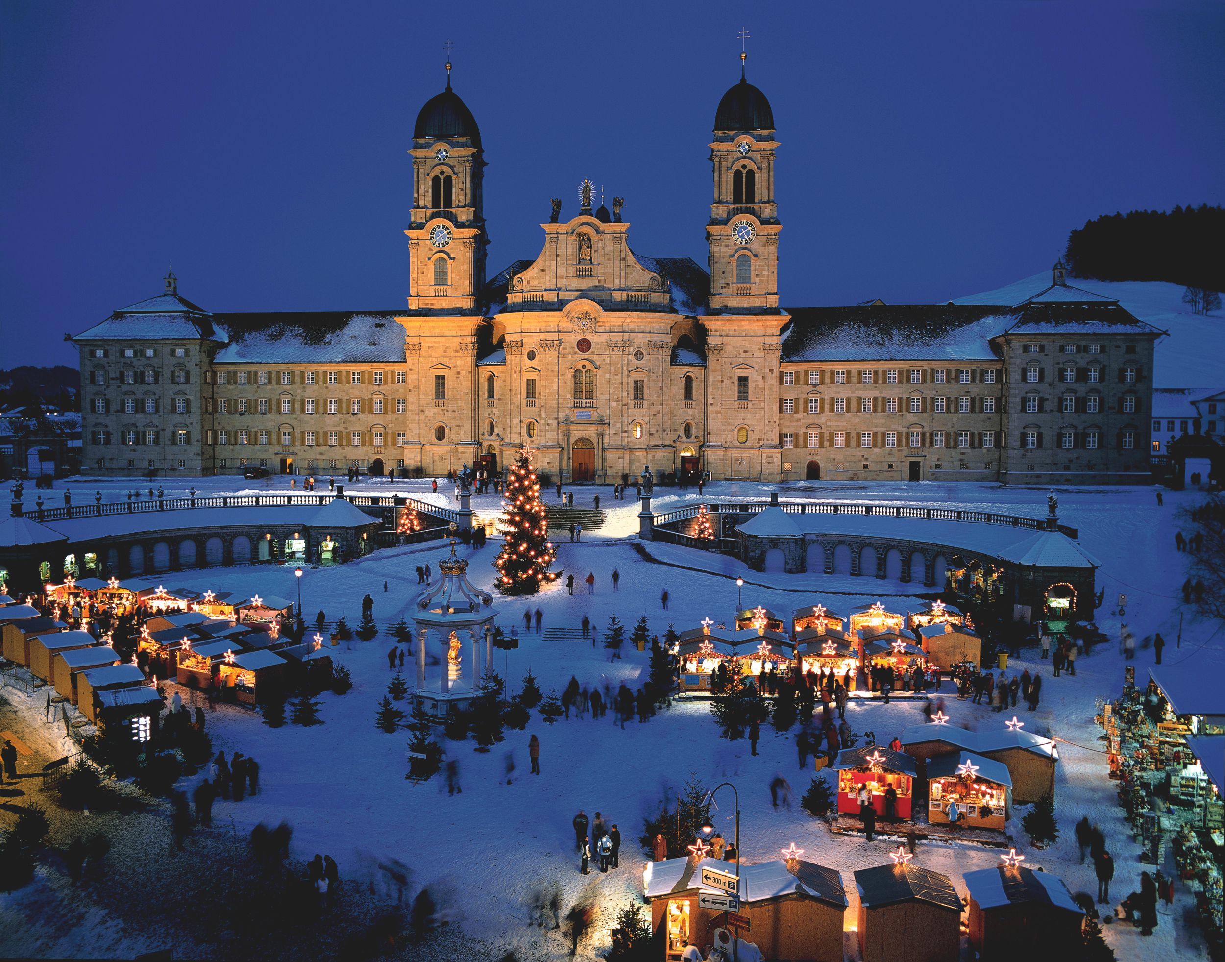 Klostertorget: festlig julstämning med marknad, kloster Einsiedeln och snötäckta landskap.