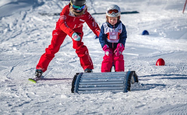 Kinder Skiunterricht in Grindelwald mit einem Lehrer, der einem Mädchen hilft. Schnee und Skiausrüstung sichtbar.
