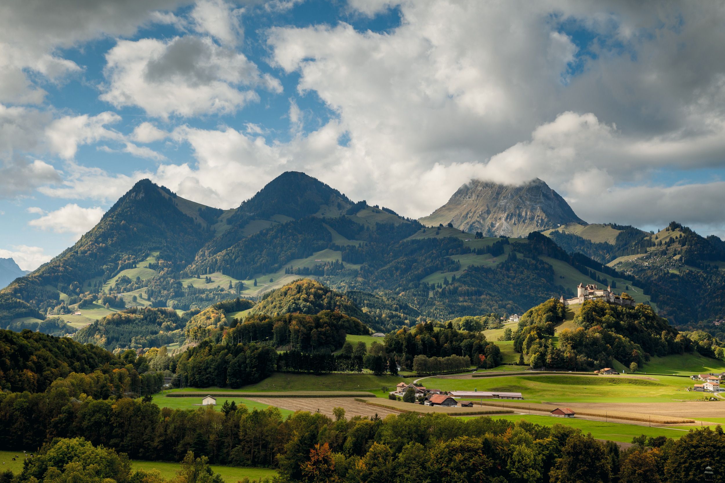 Broc-Gruyères : paysage pittoresque avec montagnes, prairies et architecture traditionnelle.