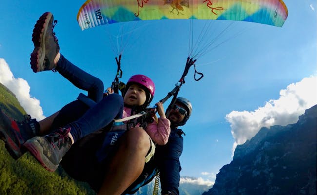 Volo in parapendio a Braunwald, bambino con elmetto, paesaggio montano sullo sfondo.