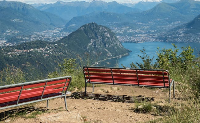 Monte San Salvatore med bank och utsikt över Lago di Lugano.