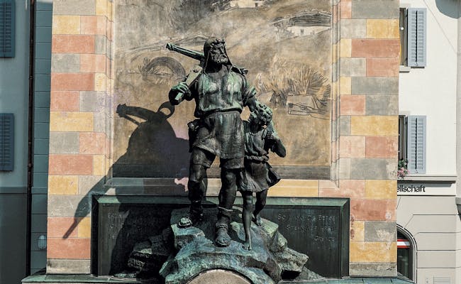 Monumento a Tell en Altdorf, Heinrich Tell con niño, estatua de bronce, entorno histórico.