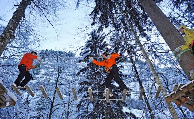 Parco avventura Engelberg con alberi coperti di neve, arrampicatori su ponti di legno
