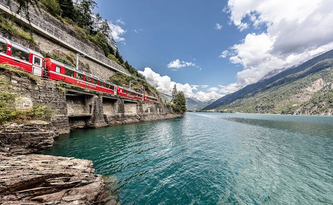 Bernina Express at Lake Poschiavo with blue water and mountains in the vicinity
