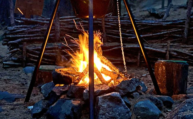 موقد نار بزيرمات مع قدر فوندو وقطع خشب بين الأشجار.