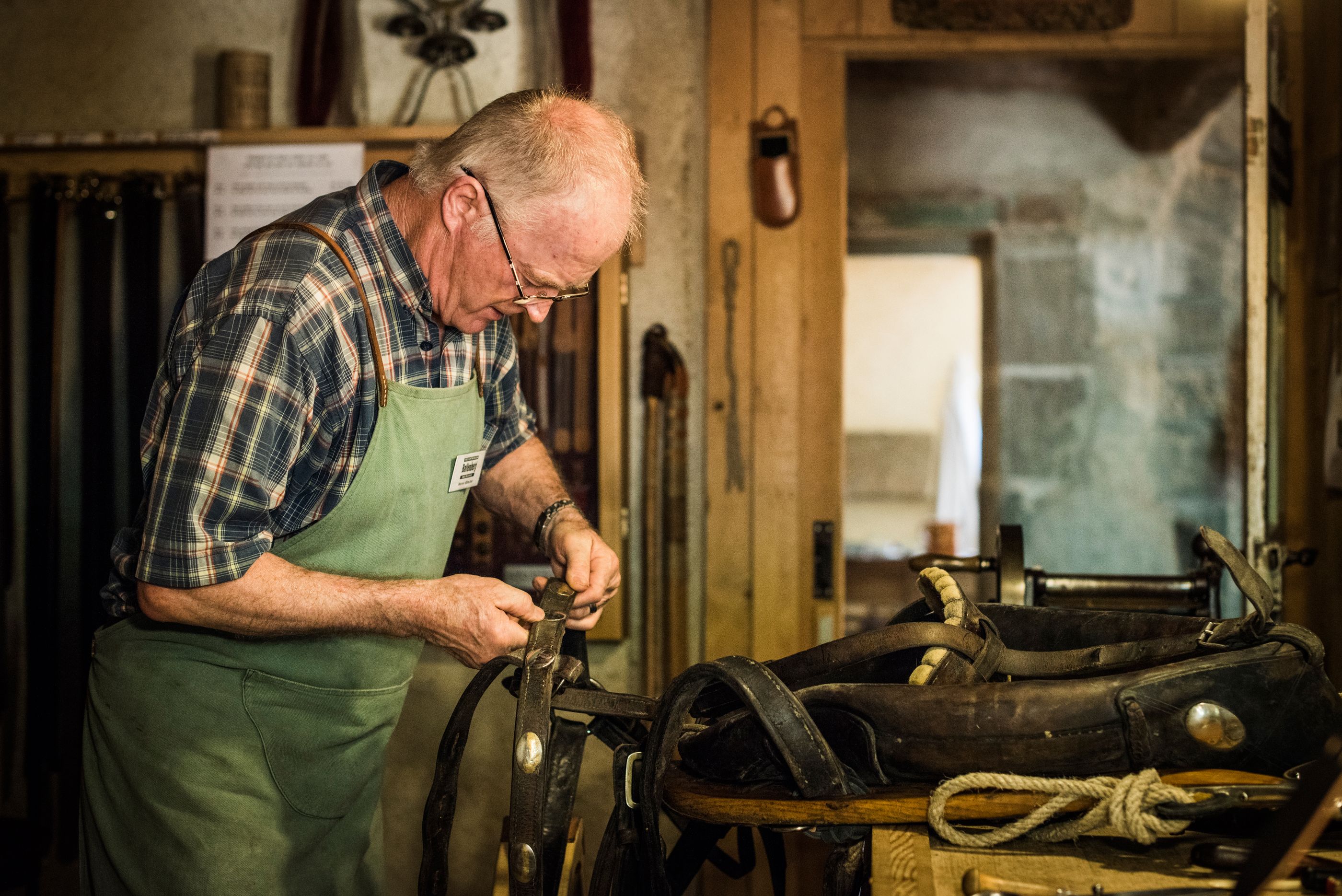 在巴伦贝格露天博物馆，一个工匠正在修理马鞍。背景中可见工具和一个工作坊。