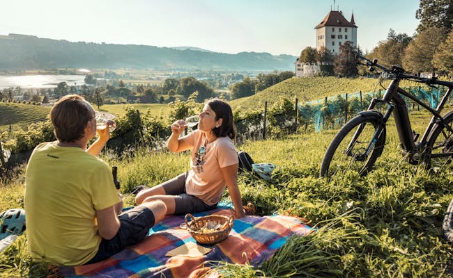 Picnic con vistas al castillo de Heidegg en Suiza en un día soleado, ciclistas al fondo