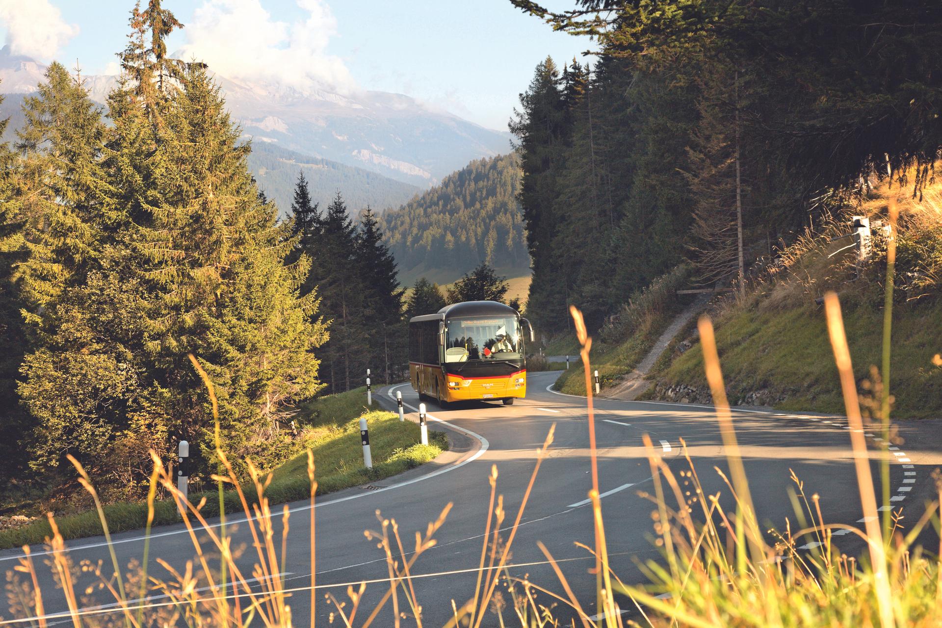 Chur: Kereta Postauto melintasi pemandangan indah di Pergunungan Alpen Switzerland dengan padang rumput hijau.