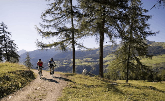 Rota de mountainbike 441 em Tarasp, ciclistas a caminho, ar fresco e prados verdes.