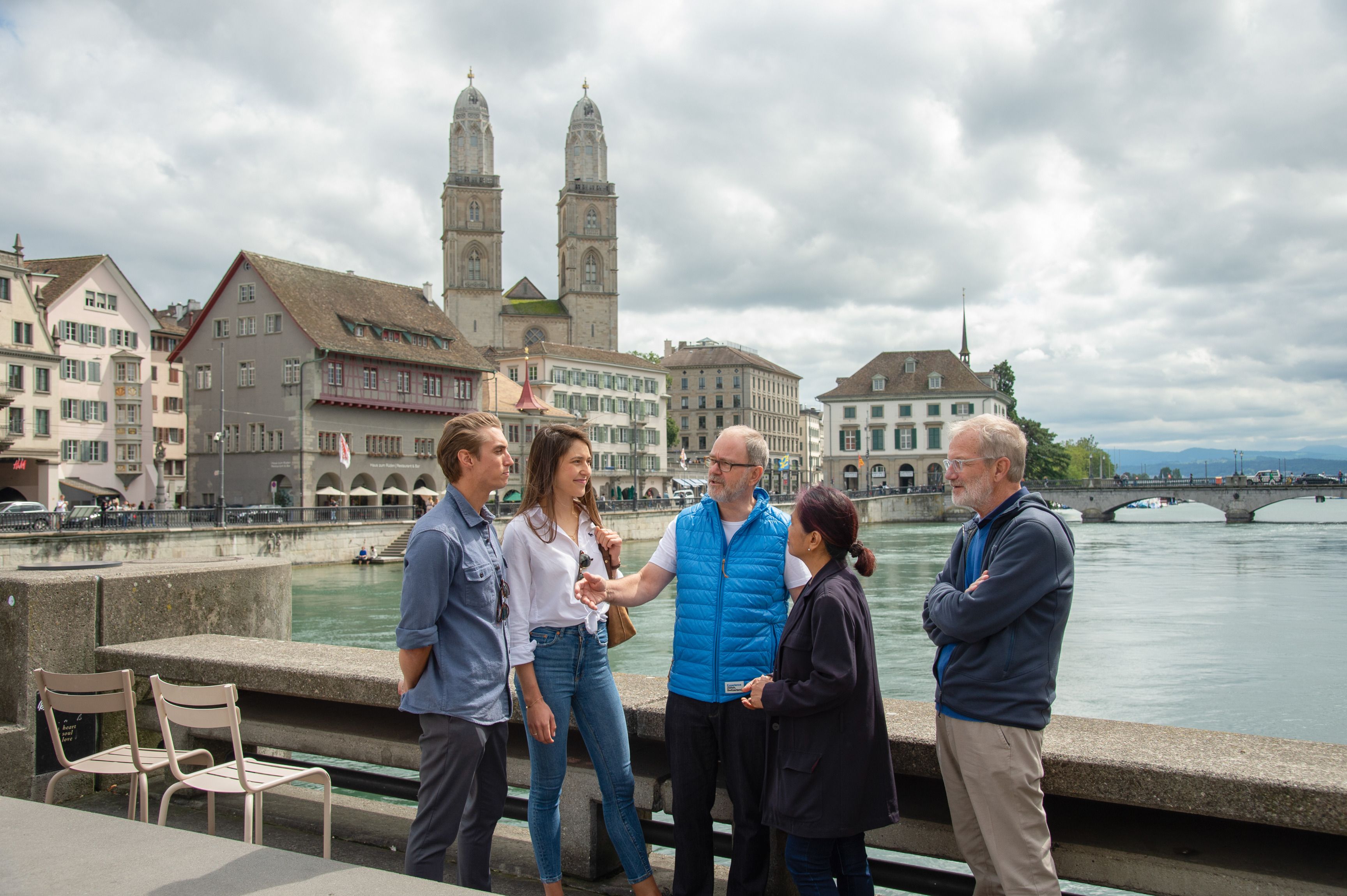 Stadsvandring i Zürcher gamla stad med grupp vid Limmat, historiska byggnader i bakgrunden.