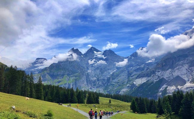 Wanderer auf dem Weg zum Oeschinensee, umgeben von Bergen und Wäldern.