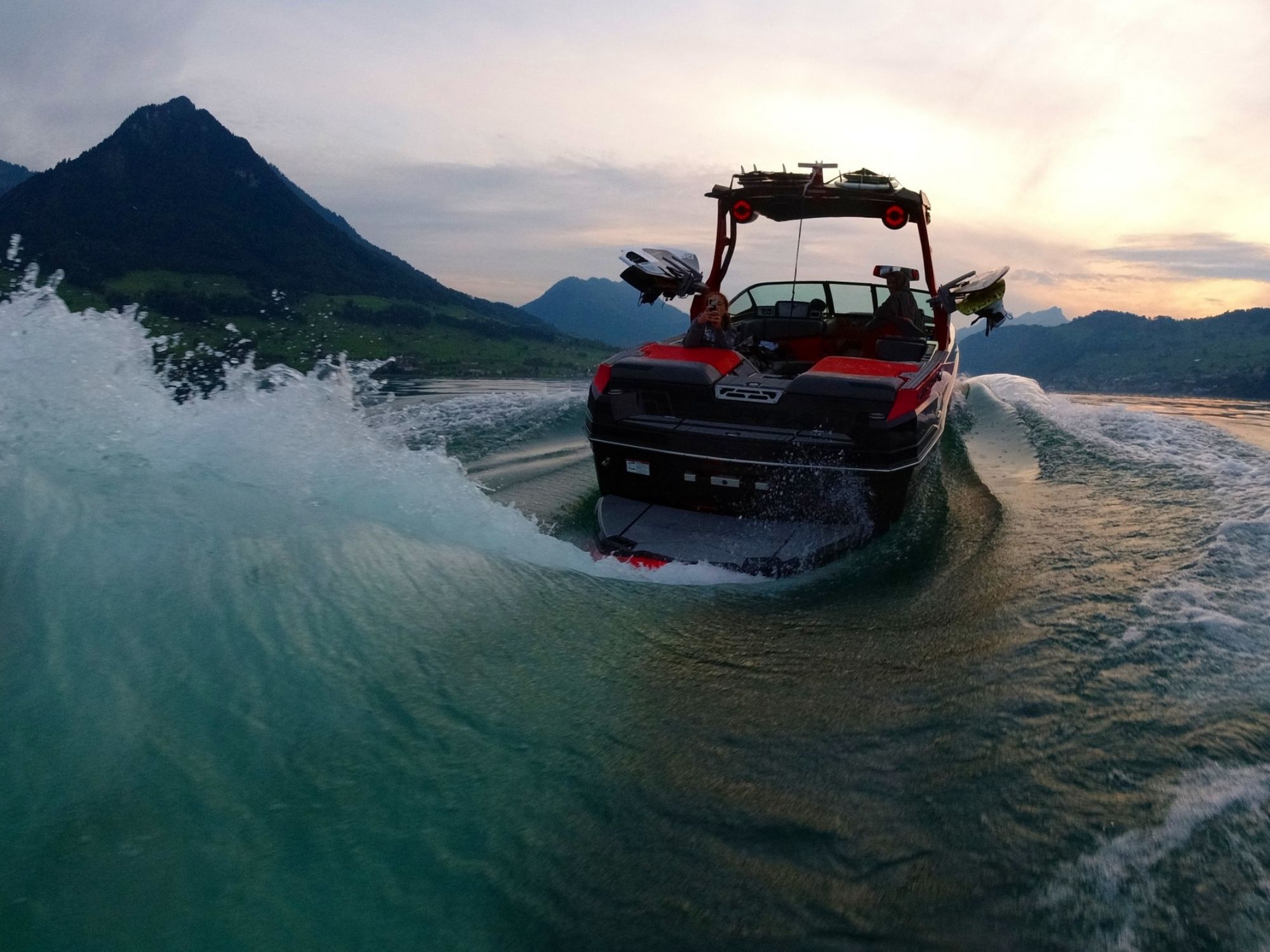 Wakeboarden op een meer met een boot en berglandschap op de achtergrond.