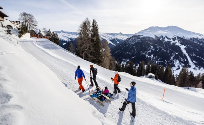 Beim Schlitteln in Davos ziehen Familien mit Schlitten die verschneite Piste hinauf.
