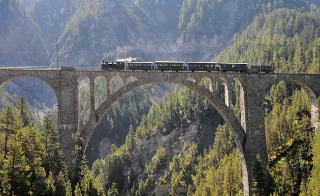 Viaduc de Landwasser des Chemins de fer rhétiques avec un train sur le pont, entouré de montagnes et de forêts.