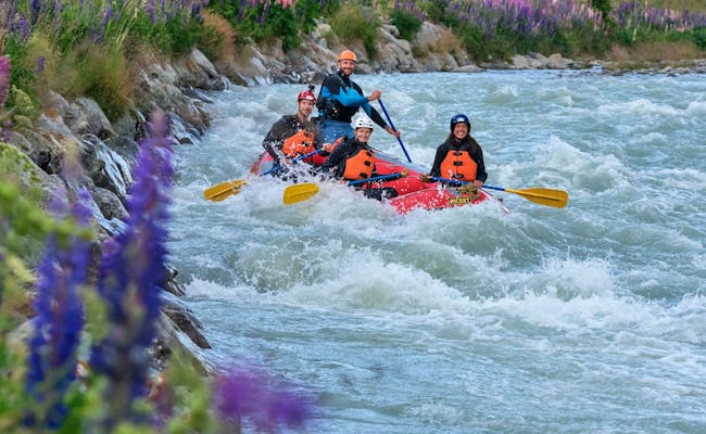 Rafting in Engadina, famiglia che pagaia attraverso un fiume selvaggio, fiori viola sulla riva