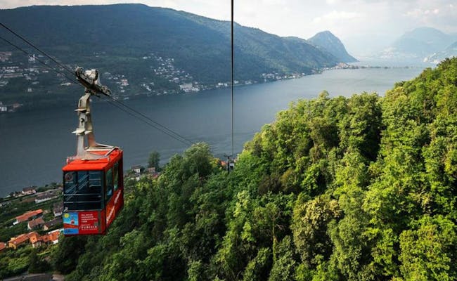 Seilbahn Brusino-Serpiano über dem Lago di Lugano, umgeben von Wäldern und Bergen.