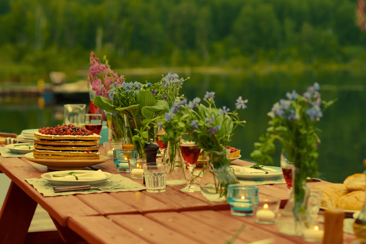 यॉट नाइटइवेंट: फूलों वाली स्टाइलिश मेज, स्वादिष्ट भोजन और पृष्ठभूमि में सौंदर्यपूर्ण झील के साथ।