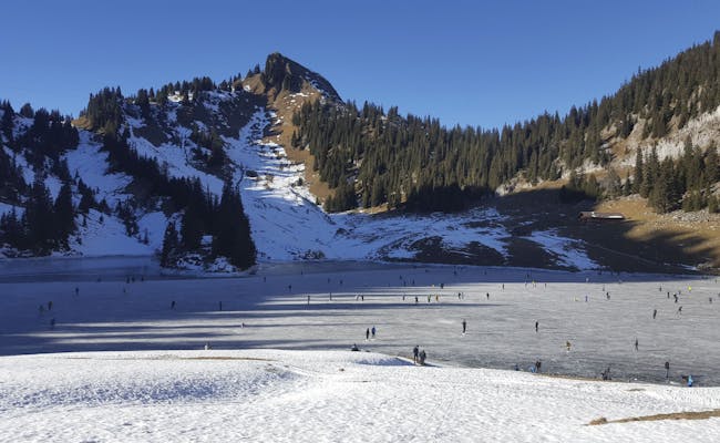 Pista de hielo natural Stockhorn con patinadores en la superficie, montañas nevadas al fondo.
