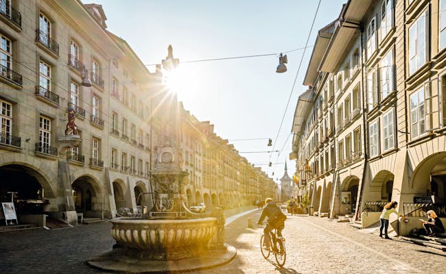 Kramgasse Berna: Vista histórica de la ciudad con ciclista y clima soleado, ideal para explorar.