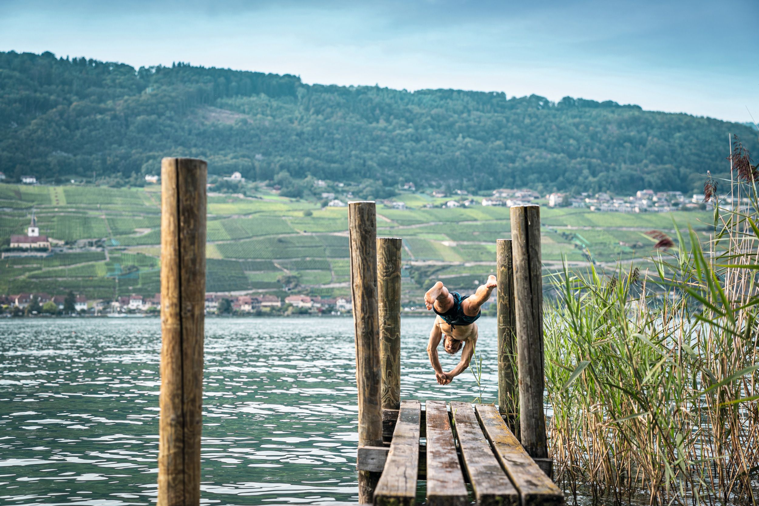 Steg sul Lago di Bienne con persona che salta in acqua. Circondario: acqua, riva, colline con vigne.